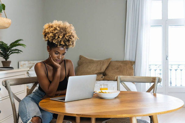 Atraktivní Atraktivní Afroameričanka sedící na židli a sledující notebook u stolu se snídaní - Fotografie, Obrázek