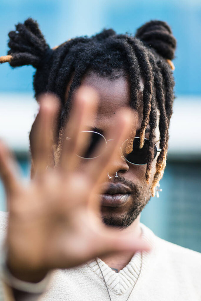 Modern African American guy with dreadlocks in buns and nose piercing outstretching hand toward camera in stop gesture - Photo, Image