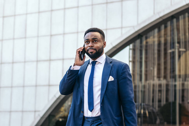 Homme noir d'affaires en costume parlant au téléphone tout en quittant le bureau - Photo, image