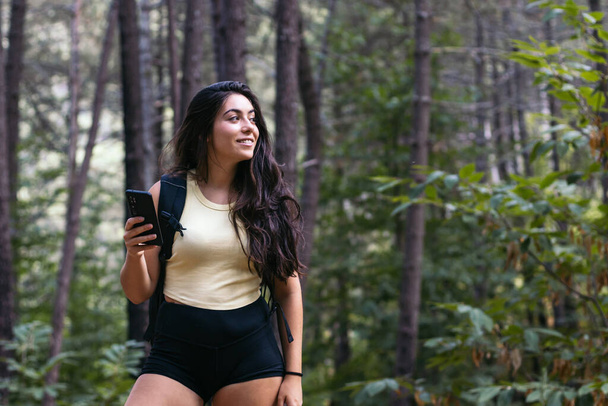 Fiatal vidám nő túrázás az erdőben, és okostelefon használata - Fotó, kép