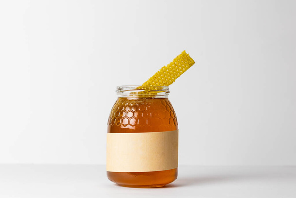 Stukje honingraat op glazen pot vol verse natuurlijke gouden honing met witte achtergrond - Foto, afbeelding
