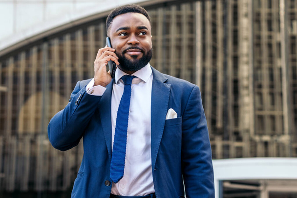 Uomo nero in giacca e cravatta che parla al telefono mentre lascia l'ufficio - Foto, immagini