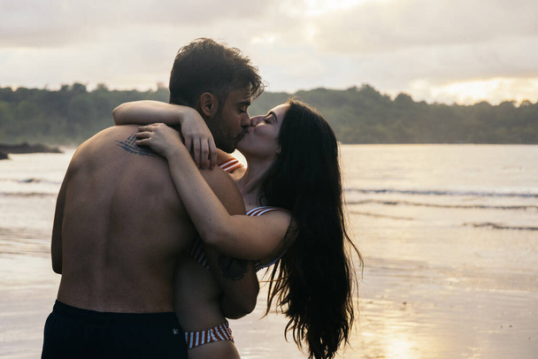 Романтичне фото пари, яка цілується на пляжі, дивлячись захід сонця - Фото, зображення