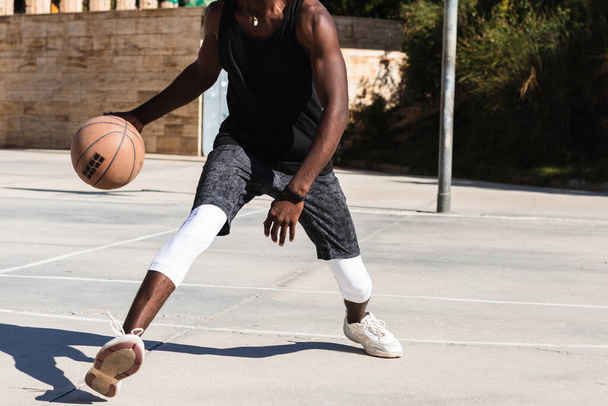 Обрезанный непризнанный афроамериканский спортсмен, играющий в баскетбол на площадке летом и смотрящий в камеру - Фото, изображение