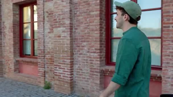 Selbstbewusster junger Hipster-Mann in grünen Klamotten, der mit dem Fahrrad über ein modernes Gebäude an der Stadtstraße läuft. Umweltfreundliches Verkehrs- und Pendlerkonzept. - Filmmaterial, Video