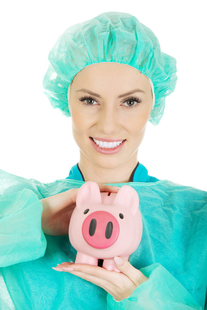 Female doctor with pink piggy bank. - 写真・画像