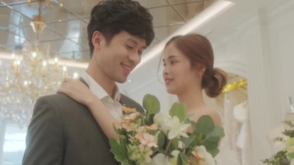 花は密かに花束を花に与える. 若いアジアのカップルは,ブライダルストアでフィッティングルームでの結婚式のための準備を楽しんでいます. - 映像、動画