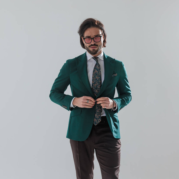 Porträt eines selbstbewussten, eleganten Mannes mit Sonnenbrille, grünem Anzug und vor grauem Hintergrund  - Foto, Bild