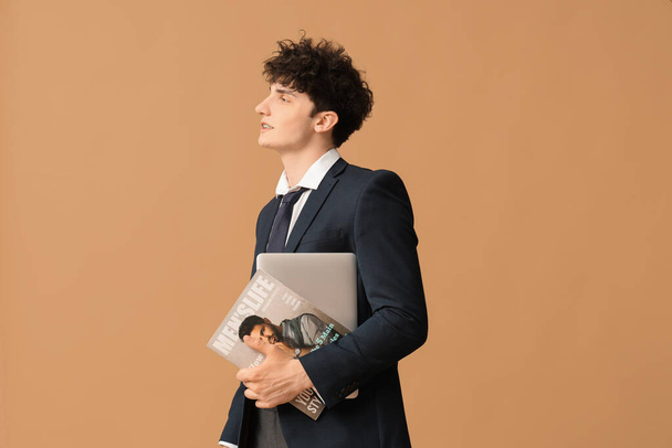 Handsome young businessman with modern laptop and magazine on brown background - Φωτογραφία, εικόνα