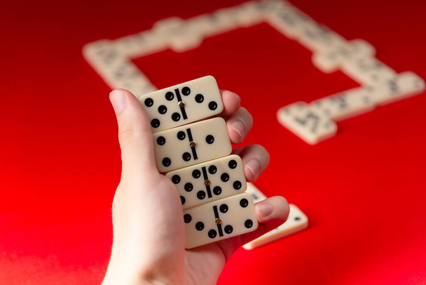 Jugador dominó sosteniendo piezas acrílicas de número rectangular. Juego de mesa. Fondo rojo. - Foto, Imagen