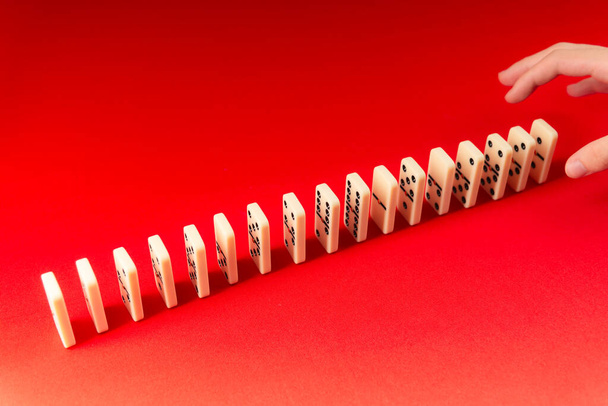 Mano masculina colocando las piezas en una fila para el efecto dominó. Aislado sobre fondo rojo. - Foto, Imagen