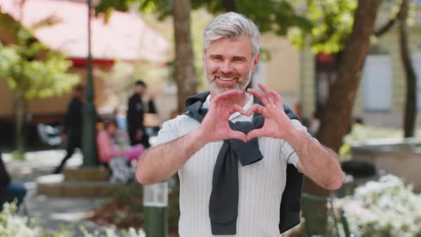 Ben de seni seviyorum. Beyaz, orta yaşlı bir adam kameraya kalp işaretini gösteren bir aşk sembolü yapar, samimi, romantik, olumlu hisler ifade eder. Sadaka, minnettarlık, bağış. Şehir parkında olgun bir adam.. - Video, Çekim