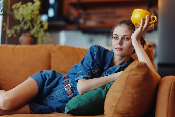 Boldog nő élvezi egy csésze kávét egy kényelmes kanapén otthon egy mosollyal az arcán - Fotó, kép