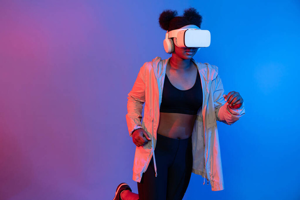 Fiatal afrikai sport nő visel VR futó pózol kék neon világítás élénk összekötő digitális futurisztikus technológia virtuális valóság metaverse világ gyakorlat esports digitális egészség. Vállalkozás. - Fotó, kép