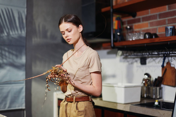 Žena stojící v kuchyni drží závod v ruce obklopen přirozeným světlem a moderní výzdobou - Fotografie, Obrázek