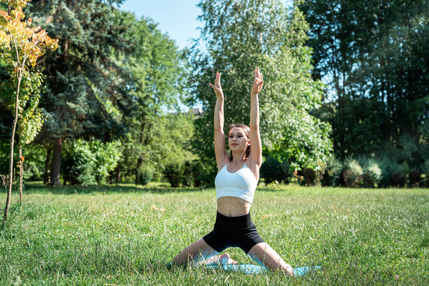 Entraîneur de fitness féminin faisant des exercices de yoga matinal dans l'herbe verte au parc. L'heure d'été pour le sport. Entraînement à la nature - Photo, image