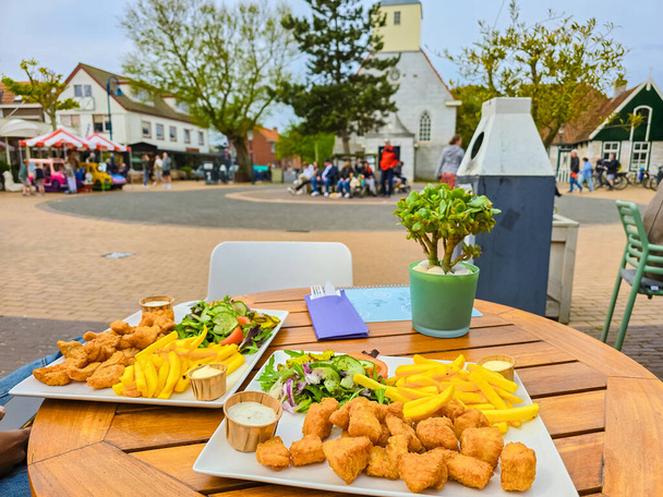 Kaksi kauniisti järjestettyä lautasellista ruokaa istuu pöydällä Texelin vilkkaalla aukiolla Alankomaissa, valmiina nälkäisten ruokailijoiden nautittavaksi.. - Valokuva, kuva