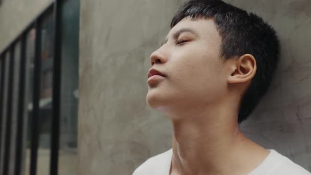 Aasialainen väsynyt järkyttynyt poika seisoo harjoittelun jälkeen lähellä seinää. Nuori masentunut kaveri tuntee yksinäinen ulkona ja haaveilee. Ihmiset ja tunteet käsite - Materiaali, video