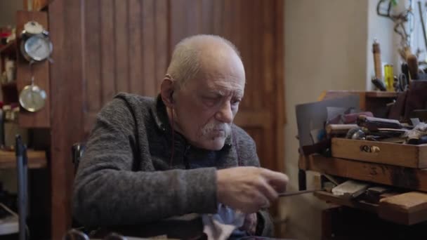 Senior harmaa tukka uros mestari pyörätuolissa työskentelee hänen työpaja teroitus japanilainen miekat terä - Materiaali, video