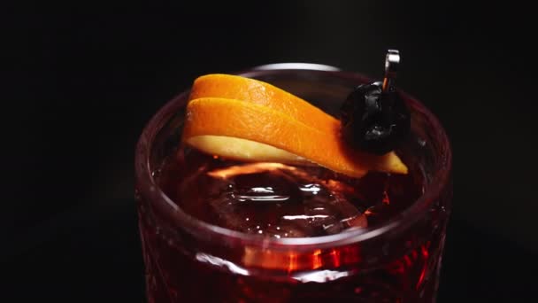 Overhead άποψη για κλασικό ποτό negroni γαρνιρισμένο με ξύσμα πορτοκαλιού φλούδα και μαύρη ελιά σε σουβλάκι. Διακόσμηση λεπτομερειών παλιομοδίτικου cocktail με παγάκια σε ποτήρι. - Πλάνα, βίντεο