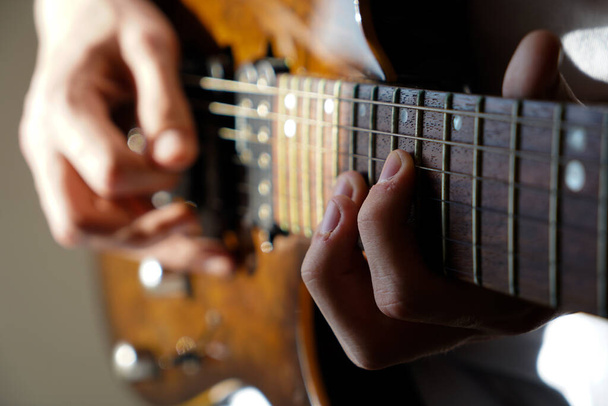 Руки кавказького музиканта, який грає на електрогітарі, грає на яскраво-коричневій дерев'яній електрогітарі - Фото, зображення