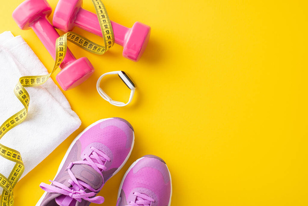 Flat lay of pink fitness equipment including dumbbells, shoes, measuring tape, and a towel on a vibrant yellow background - Foto, Imagem