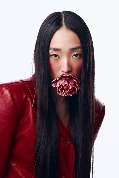 Glamorous woman in red jacket with flower in mouth posing with long black hair - Photo, Image