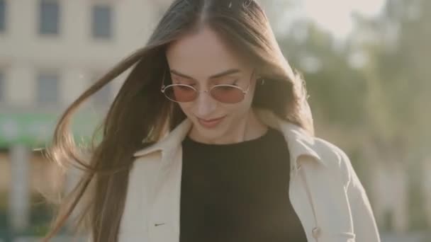 Eine junge Frau genießt einen sonnigen Tag in der Stadt, trägt eine stylische Sonnenbrille und lächelt selbstbewusst. Lächelnde Frau mit Sonnenbrille draußen in der Stadt - Filmmaterial, Video