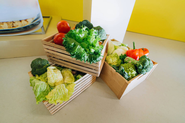 Деревянная коробка с овощами: капуста, перец, брокколи, лук, помидор, зеленый салат. Фермерская ярмарка с продажей овощей - Фото, изображение