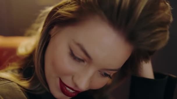 Close-up of a smiling woman with red lipstick and long hair, looking downwards in a warm, soft light. Beautiful Woman with Red Lipstick Smiling and Looking Down. Young Beautiful Woman. - Video