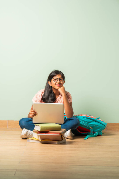 Indiai ázsiai iskolás lány alkalmi viselet segítségével laptop tanulmány ül a padlón elszigetelt - Fotó, kép