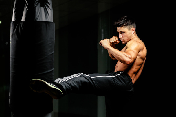muscular fighter leg middle kick to heavy bag - Foto, Imagen
