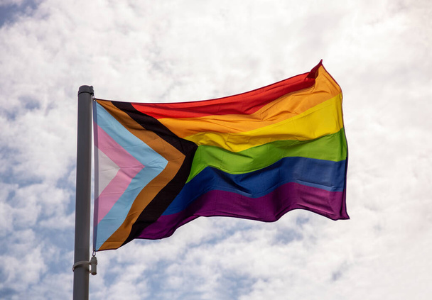 Gay σημαία υπερηφάνεια φτερουγίζει στο αεράκι ενάντια σε ένα συννεφιασμένο καλοκαιρινό πρωινό ουρανό - Φωτογραφία, εικόνα