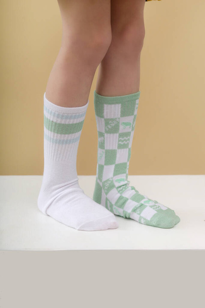Kind trägt verschiedene Socken. Kinderfüße in unpassenden Socken, Studioaufnahmen. Down-Syndrom-Aufklärungskonzept, seltsamer Socken-Tag, Anti-Mobbing-Woche. - Foto, Bild