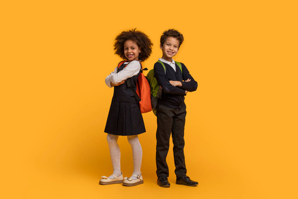 Okul üniforması giymiş iki Afro-Amerikalı çocuk parlak sarı bir arka planda duruyorlar. Kuyrukta bekliyor gibi görünüyorlar, gözleri ileride. - Fotoğraf, Görsel