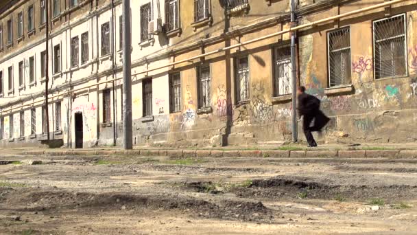 Un joven con un abrigo negro corre entre los viejos edificios - Metraje, vídeo