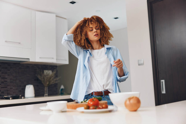 Жінка з кучерявим волоссям, що стоїть на кухні з тарілкою їжі на стійці - Фото, зображення