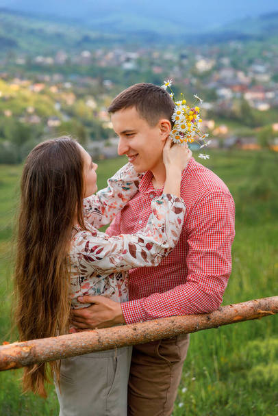 A young couple is standing face to face. The girl tenderly embraces the guy by the neck and holds a bouquet of flowers . Tenderness shines in their eyes. - Photo, Image