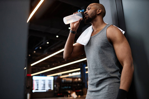 Side view portrait of muscular Black man drinking water after training in gym interior, copy space - Photo, Image