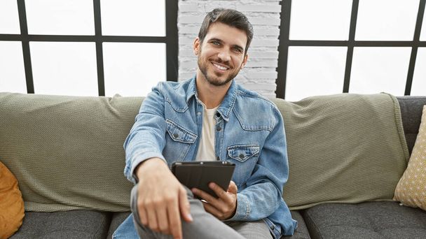 Przystojny Latynos uśmiechający się tabletem w nowoczesnym salonie - Zdjęcie, obraz