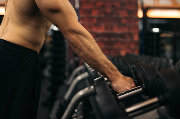 Сильный мужчина без рубашки поднимает гантель в спортзале - Фото, изображение