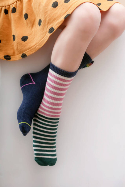 Kind trägt verschiedene Socken. Kinderfüße in unpassenden Socken, Studioaufnahmen. Down-Syndrom-Aufklärungskonzept, seltsamer Socken-Tag, Anti-Mobbing-Woche. - Foto, Bild