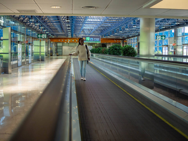 A young woman on a moving walkway inside an airport using her phone - Фото, зображення
