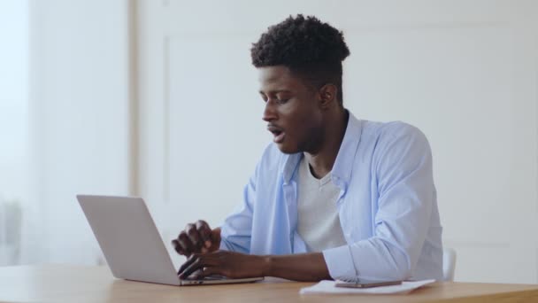 Έννοια υπερεργασίας. Κουρασμένος Αφροαμερικάνος που χασμουριέται στο χώρο εργασίας, δακτυλογραφεί στο λάπτοπ στο σπίτι - Πλάνα, βίντεο