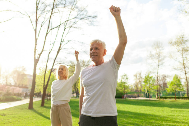 elderly couple of seniors man and woman doing exercises and training in the park outdoors, gray-haired grandparents playing sports and active lifestyle in nature - Photo, Image
