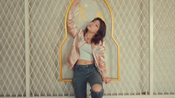 Stijlvolle jonge vrouw poserend met een speelse houding voor een getextureerde muur met geometrische patronen overdag - Video