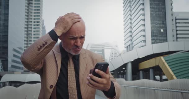 El hombre de negocios se aferra a la cabeza de dolor cuando ve una pantalla de teléfono móvil de mensaje. La expresión en la cara indica una gran angustia en el mensaje de contenido. Noticias desagradables que causaron una poderosa ola de dolor en el hombre - Imágenes, Vídeo