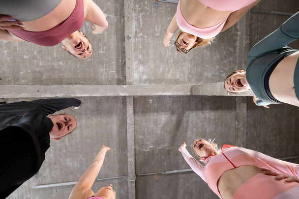 Viewed from a unique underfoot perspective, this image shows a circle of women, possibly a sports or workout team, in mid-cheer, exuding exuberance and team spirit. Their faces are expressive, with - Fotoğraf, Görsel