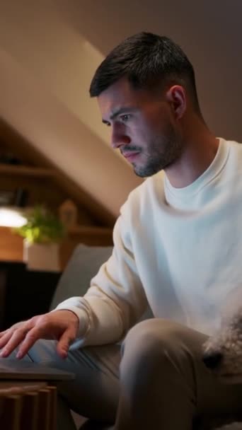 Um homem com barba está sentado em um sofá, usando um computador portátil com o polegar. Sua mandíbula está descansando em sua mão, vestindo óculos para se divertir - Filmagem, Vídeo