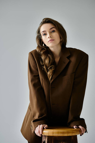Una joven embarazada con un traje marrón sentada en un taburete, exudando confianza y fuerza. - Foto, imagen